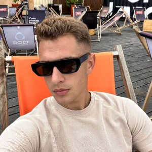 model z okularami vibe black w beżowej koszulce na pomarańczowym leżaku