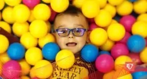 chłopiec w okularach z filtrem światła niebieskiego leżące w plastikowych kulkach